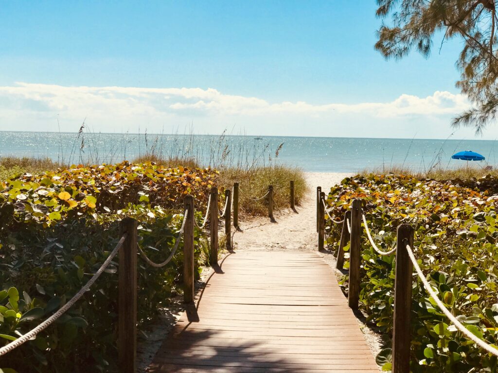 Wooden boardwalk leading through sea grapes to a Sanibel Island beach