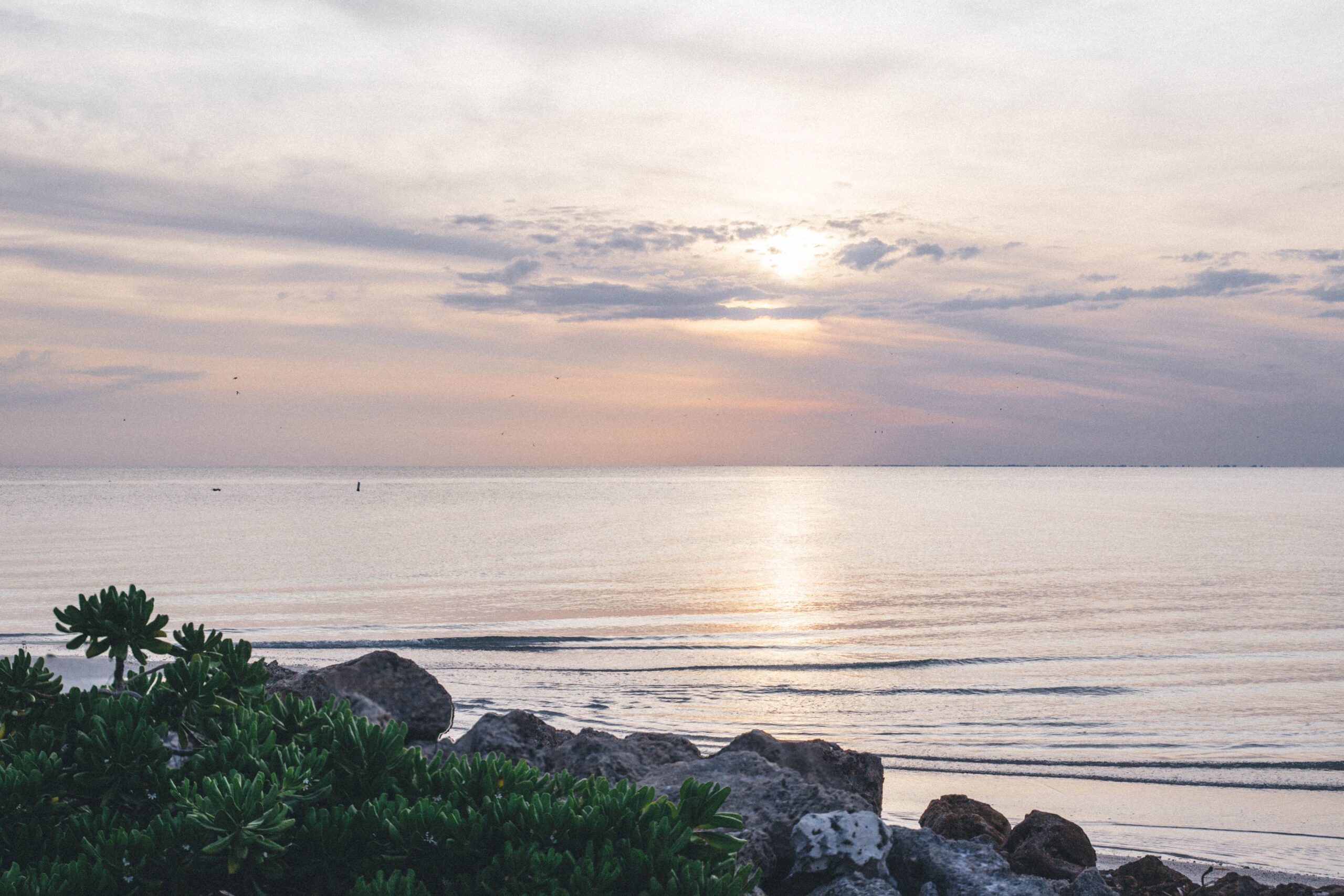 Sunset over calm Gulf waters from a rocky Sanibel shoreline